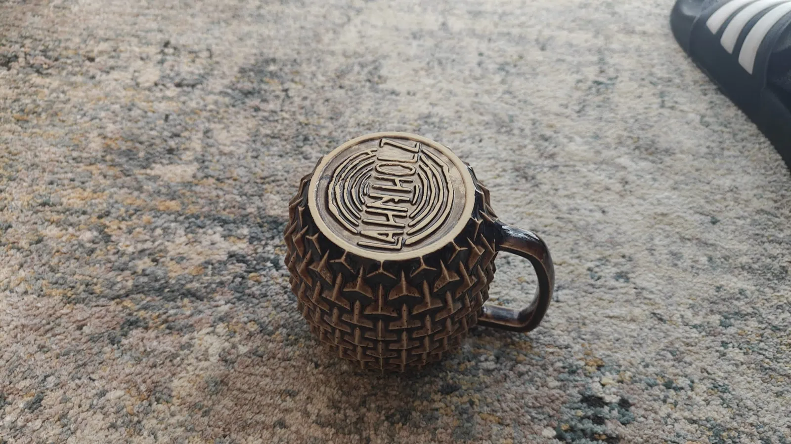 Umgedrehte dunkle Tasse: das Logo im Boden zeichnet sich ab, weil die Glasur sich in den Vertiefungen sammelt.