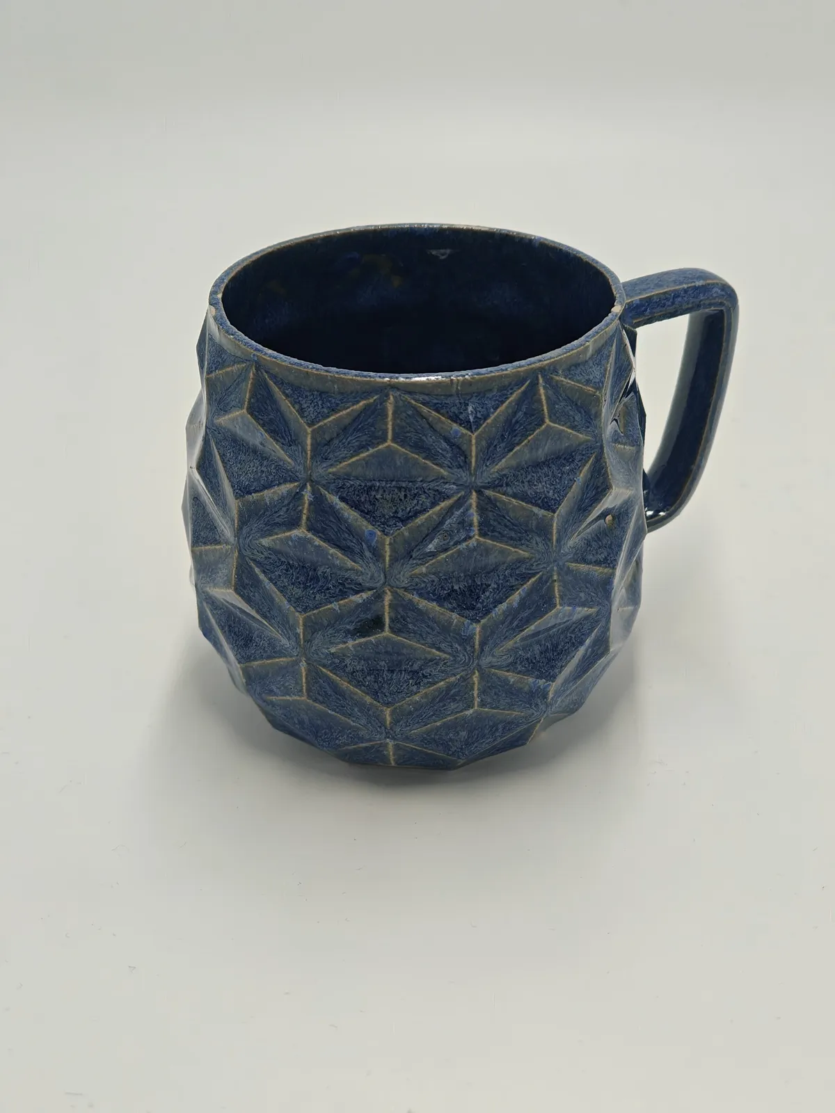 Dreieck-Tasse aus Keramik mit umlaufenden dreieckigen Facetten, gesprenkelt blau glasiert, mit eckigem Henkel.