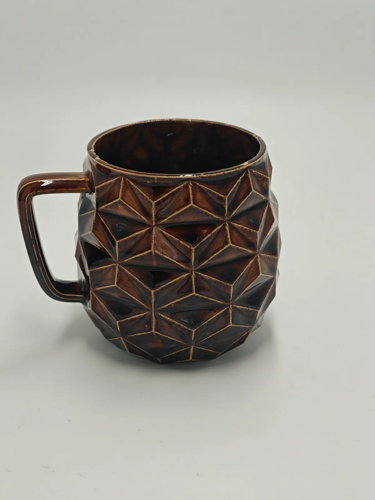 Dreieck-Tasse mit dreieckigen Facetten in glänzend brauner Schildpatt-Glasur, die sich in den Vertiefungen dunkel sammelt.