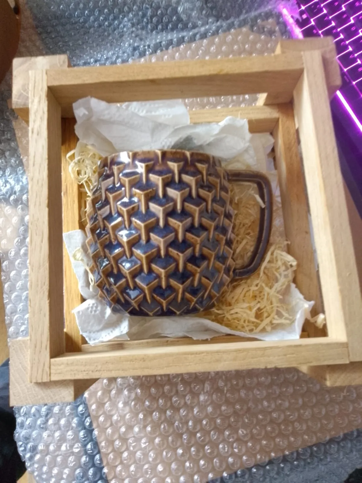 Tasse in Holzwolle gebettet in einer Geschenkbox aus hellen Holzleisten.