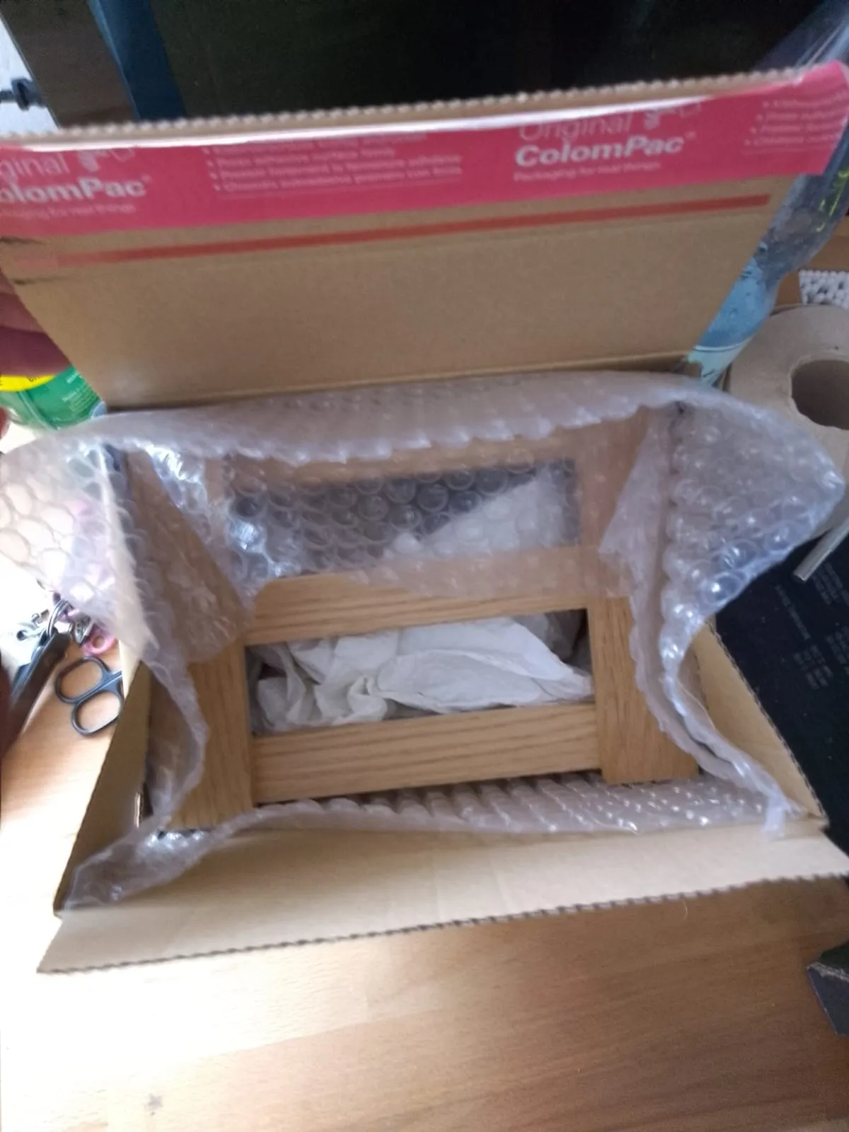 Die Holzbox, in Luftpolsterfolie gewickelt, liegt in einem geöffneten Versandkarton.